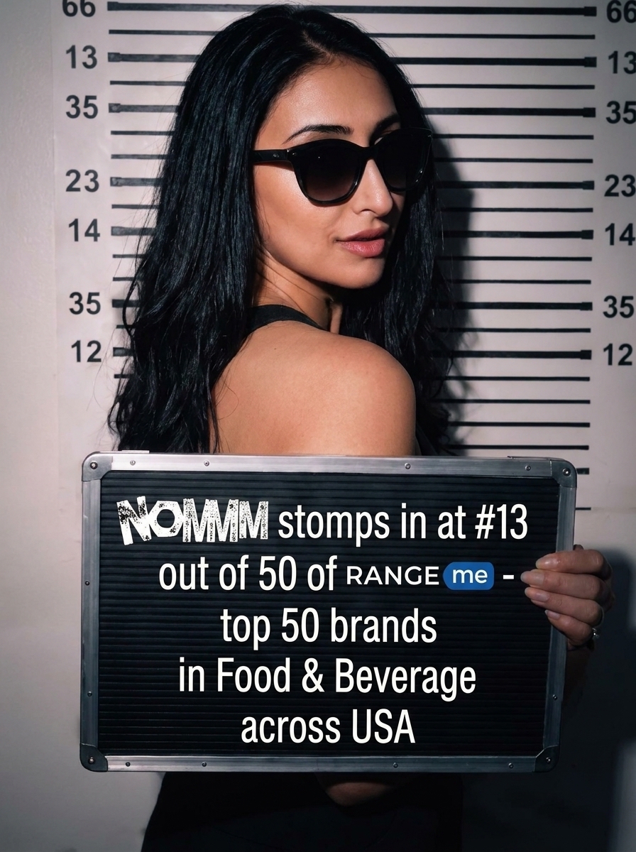 Lisa Sohanpal holding a sign reading: NOMMM stomps in at #13 out of 50 of RangeMe - top 50 brands in Food & Beverage across USA.